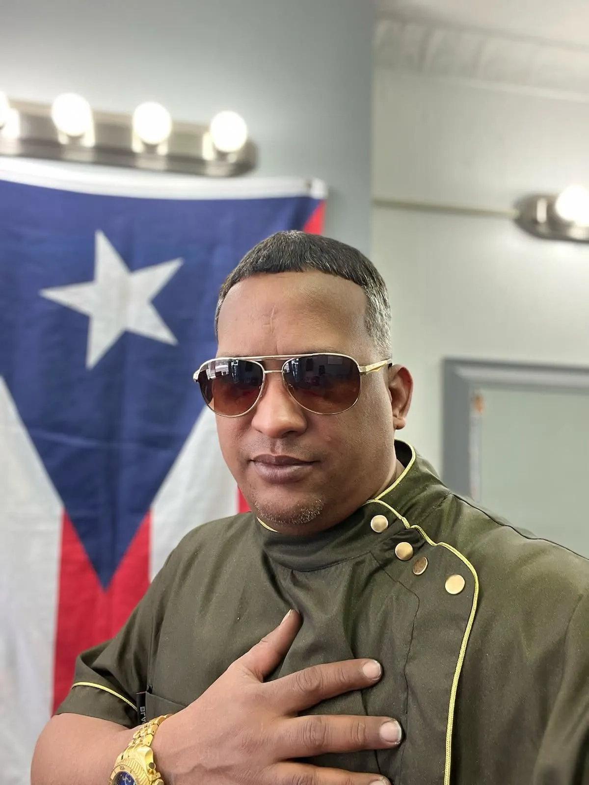 Indio Rivera, barbero licenciado, en su silla de Flawless Studio con la bandera de Puerto Rico
